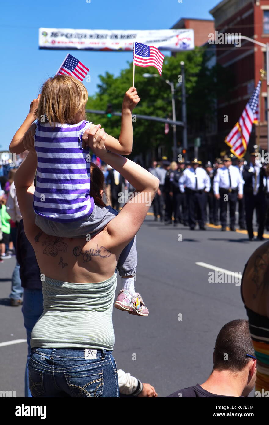 Middletown, CT USA. May 2018. Daughter sitting on mom`s shoulders waving flag during a Memorial Day celebration. Stock Photo